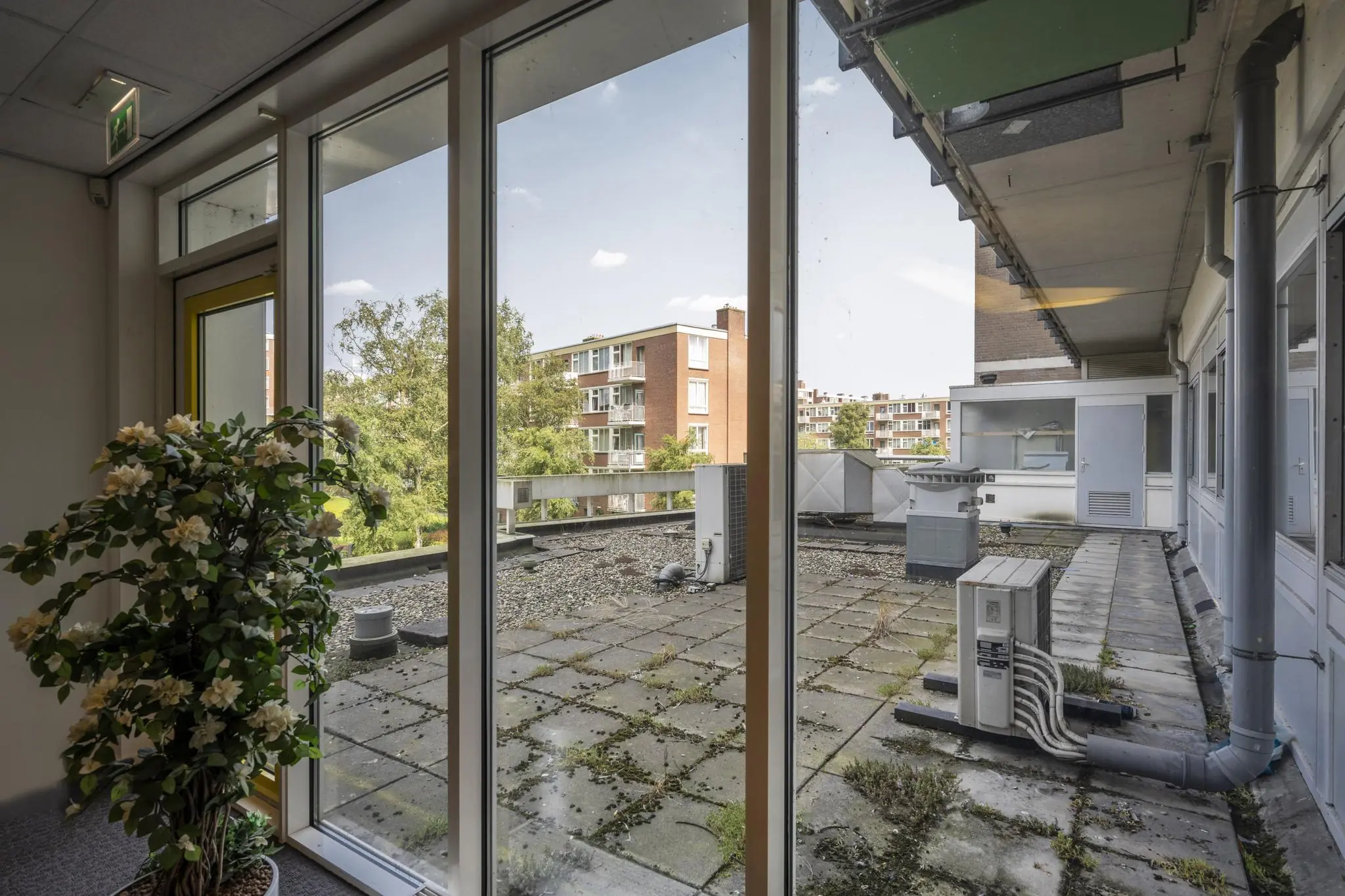 Uitzicht vanuit een kantoor aan de Jan Tooropstraat op een plat dak met ventilatiesystemen en omliggende appartementengebouwen.